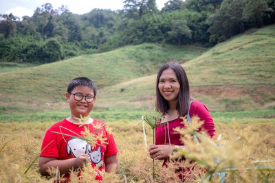 Portrait of happy woman with son standing amidst plants on land