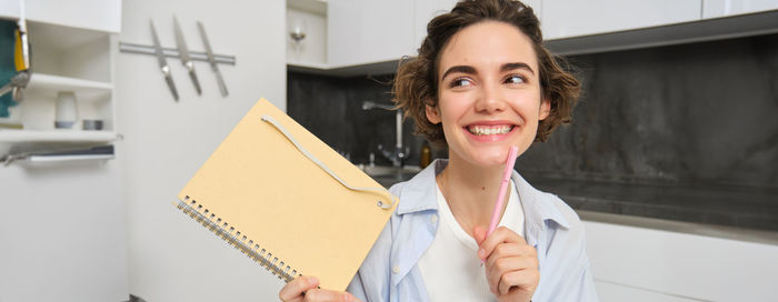 Portrait of smiling young businesswoman standing against wall