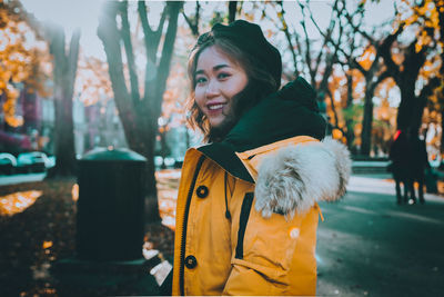 Portrait of smiling woman standing by tree during winter