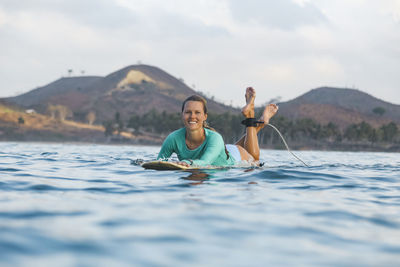 Smiling young woman lying on surfboard