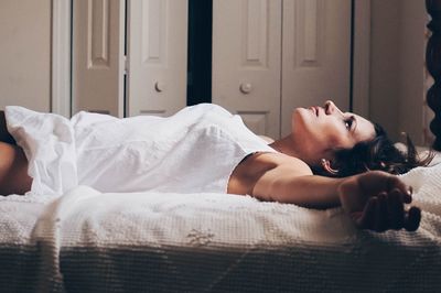 Thoughtful woman lying down on bed at home