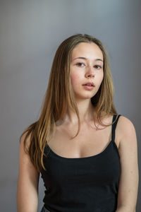 Portrait of a charming young woman wearing a camisole posing looking at camera on grey background