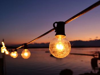 Close-up of illuminated light bulbs against sky at sunset