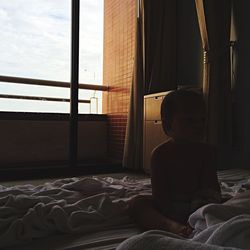 Shirtless baby sitting amidst blanket on bed at home