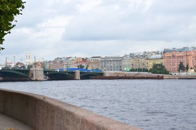 Bridge over river by buildings in city against sky