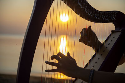 Cropped hand playing musical instrument at beach during sunset