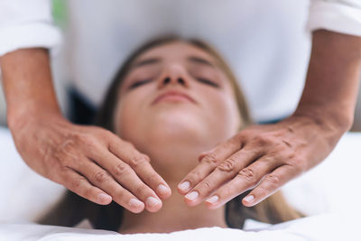 Midsection of therapist giving reiki treatment to teenage girl on face at spa