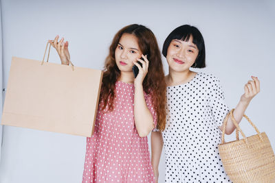 Lesbian woman talking on phone while holding bags against gray background