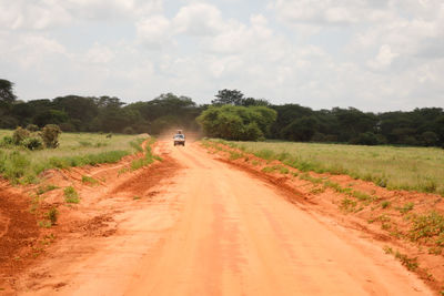 Dirt road amidst field against sky