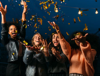 Cheerful female friends throwing confetti at night