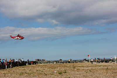 People on field against sky and helicopter 