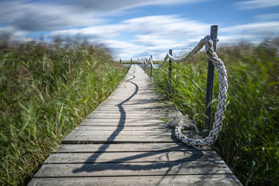 Boardwalk amidst plants on field against sky