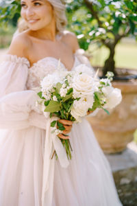 Smiling bride holding bouquet standing outdoors