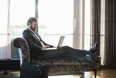 Businessman using laptop on chaise longue in hotel room