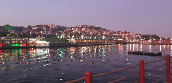 Illuminated buildings by river against sky at night