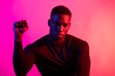 Portrait of young man standing against pink background