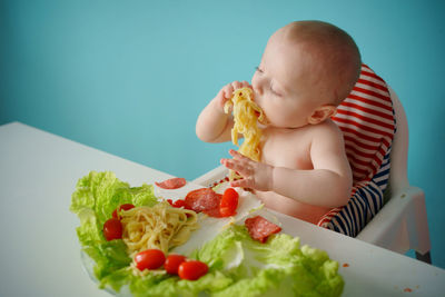 A child eats pasta with lettuce and tomatoes