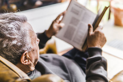 High angle view of man reading book while sitting on armchair at home