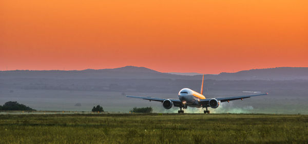 Airplane flying over runway against sky during sunset