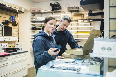 Mature female engineer using mobile phone by colleague in workshop