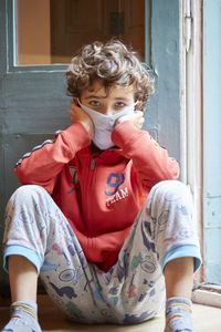 Portrait of boy wearing mask sitting against door