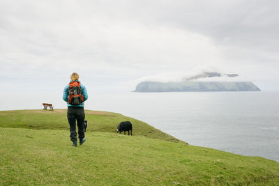 Rear view of woman with dog on grass against sky