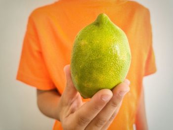 Close up view of a kid holding a green lemon