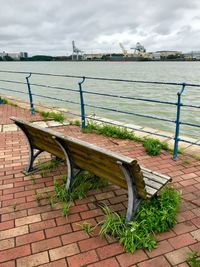 Empty bench by railing against sky