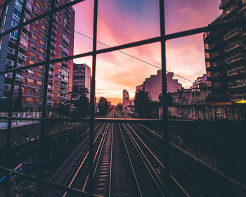 Railroad tracks in city against sky during sunset