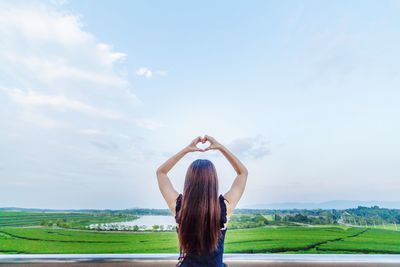 Rear view of woman making heart shape against land