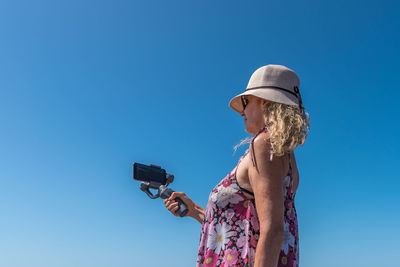 Back view of a woman using a mobile attached with a gimbal outdoors with the blue sky