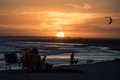 Silhouette people on beach against sky during sunset