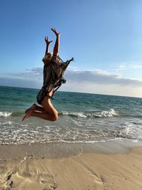 Woman jumping at beach against sky