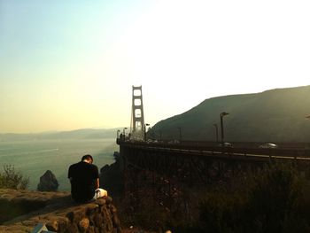 Rear view of man sitting on mountain against clear sky