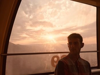Young man sitting in overhead cable car during sunset