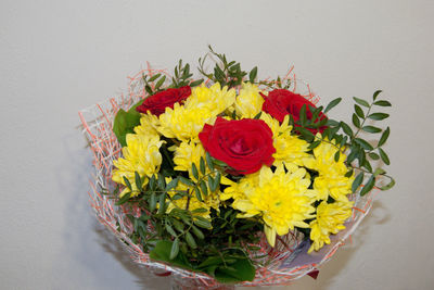 Yellow chrysanthemums and red roses in the package stands in a vase against the white wall. flowers