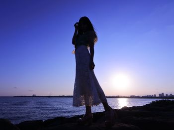 Woman standing on beach against sky during sunset