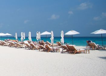 Deck chairs and parasols on sand at beach against sky