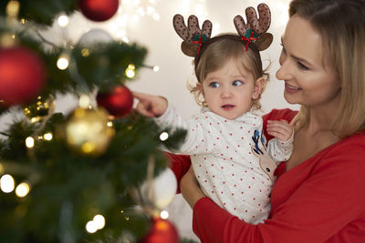 Woman carrying daughter by christmas tree