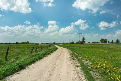 Dirt road amidst field against sky