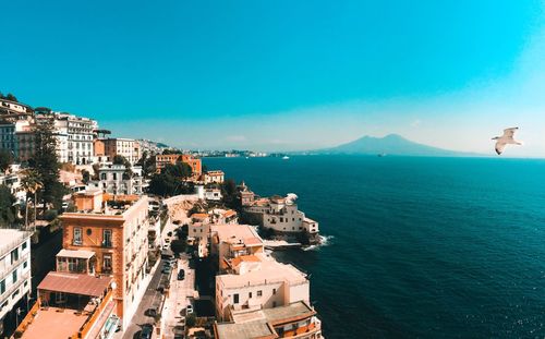 High angle view of townscape by sea against blue sky