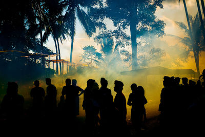 Silhouette people standing by tree against sky during sunset