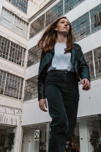 Low angle view of young woman walking against building in city