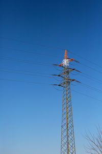 Low angle view of electricity pylon against clear blue sky