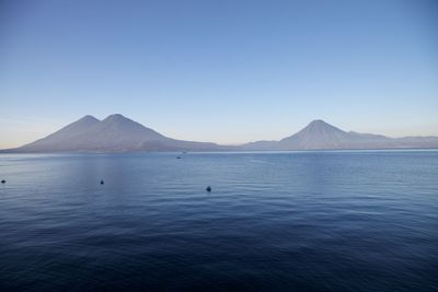 Scenic view of sea and mountains against clear blue sky