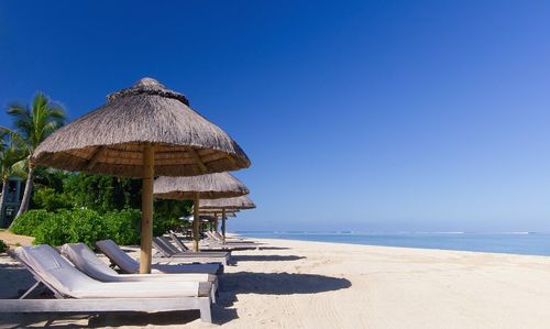 Palapas on beach against clear blue sky