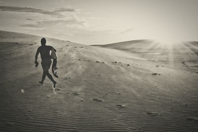 Rear view of man running on sand at desert