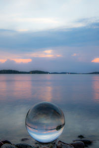 Close-up of crystal ball against lake during sunset