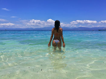 Rear view of woman wearing bikini standing in sea against sky