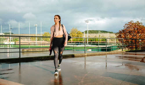 Young sportswoman with gym bag and sports shoes walking to go to training